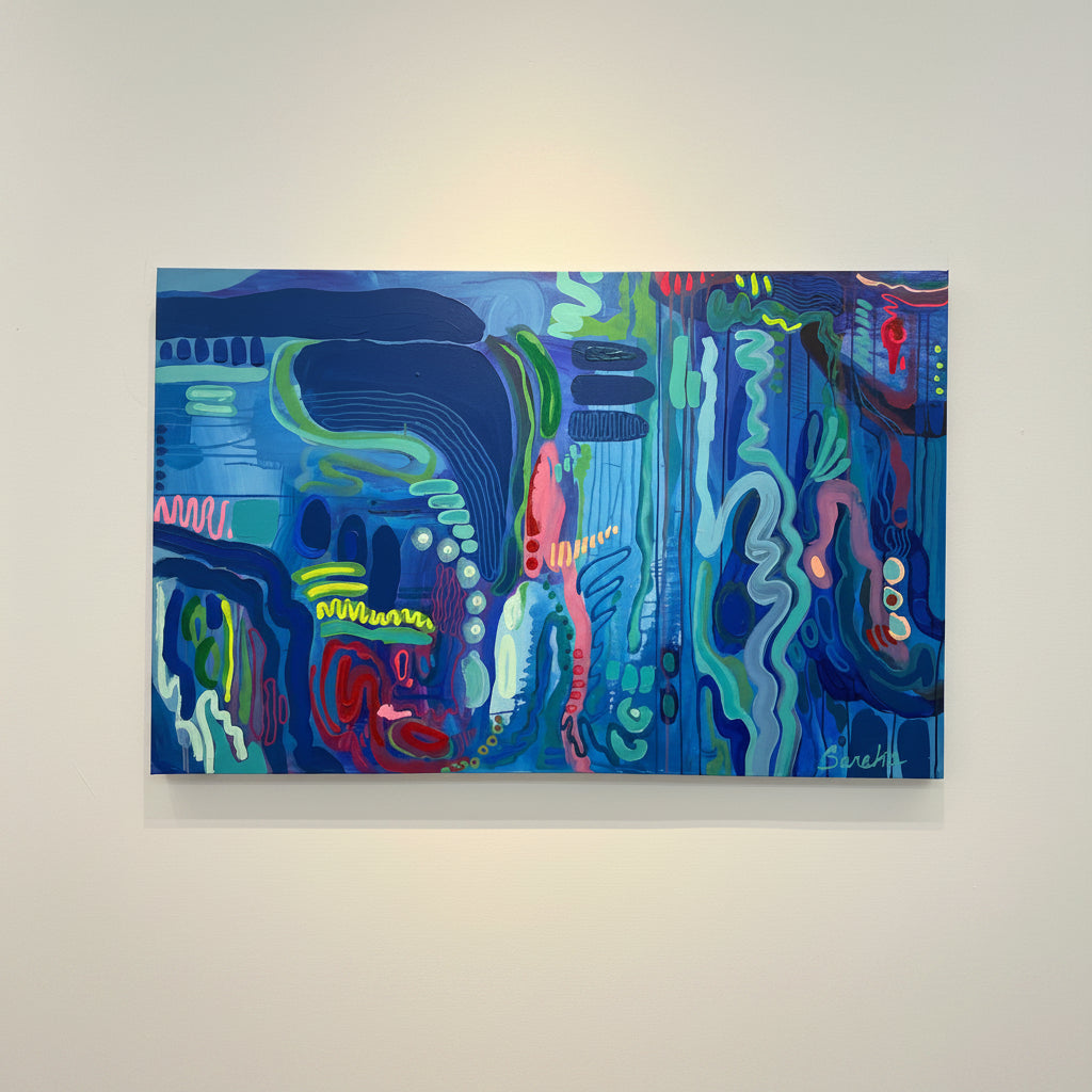 An abstract painting on a canvas, featuring a vibrant mix of blue, teal, green, pink, and red organic shapes and lines, displayed on a light beige wall.