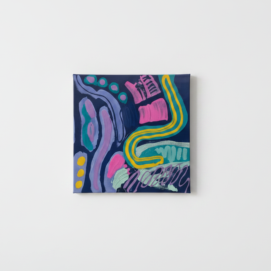 A small square abstract painting with bold pink, yellow, purple, and teal brushstrokes on a dark navy background, displayed standing on an orange table in a brightly lit art gallery with colorful paintings on the wall.