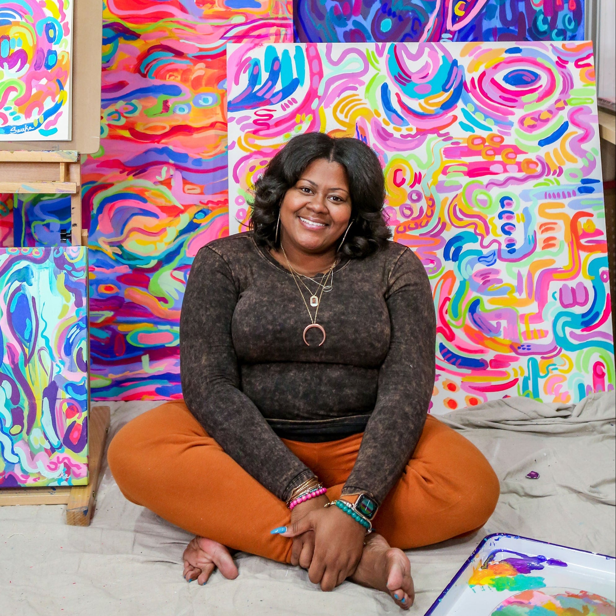 Woman sitting among colorful abstract paintings in a studio setting